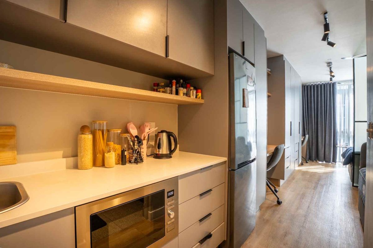 Modern galley-style kitchen featuring sleek grey cabinetry, stone countertops, integrated appliances, and efficient track lighting, seamlessly flowing into the adjacent living area.