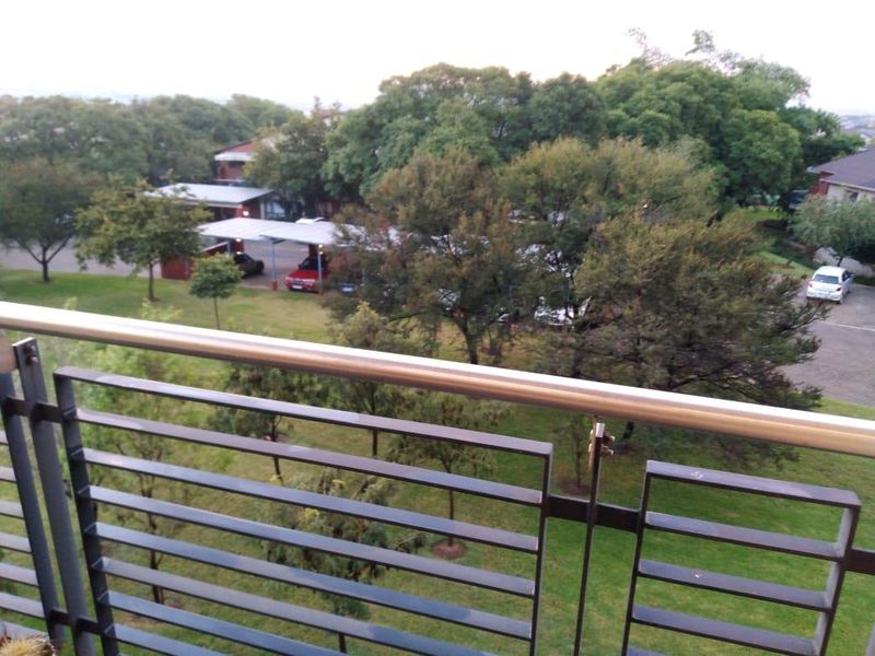 A balcony featuring a modern metal balustrade and stainless steel handrail, overlooking a landscaped garden and parking area.