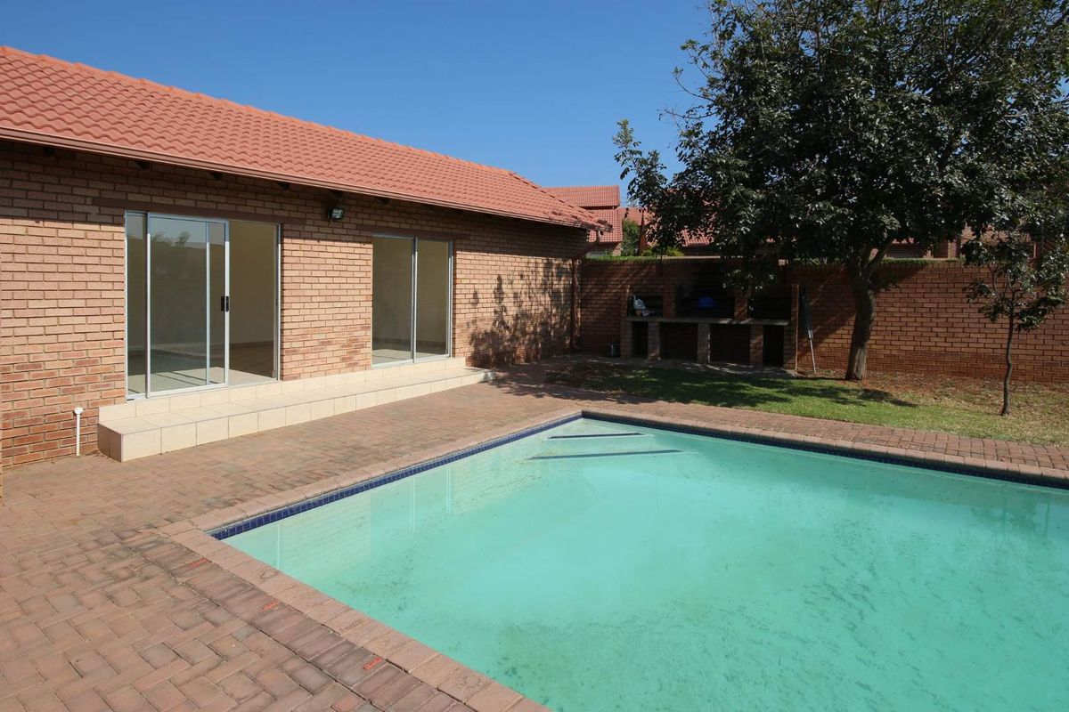 Rear exterior view featuring a swimming pool, brick paved patio area, built-in braai, and sliding door access to the main living space.