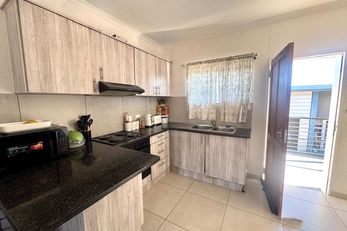 Functional kitchen featuring light wood-grain cabinetry, dark granite countertops, built-in hob, extractor fan, and double stainless steel sink with direct access to the exterior.