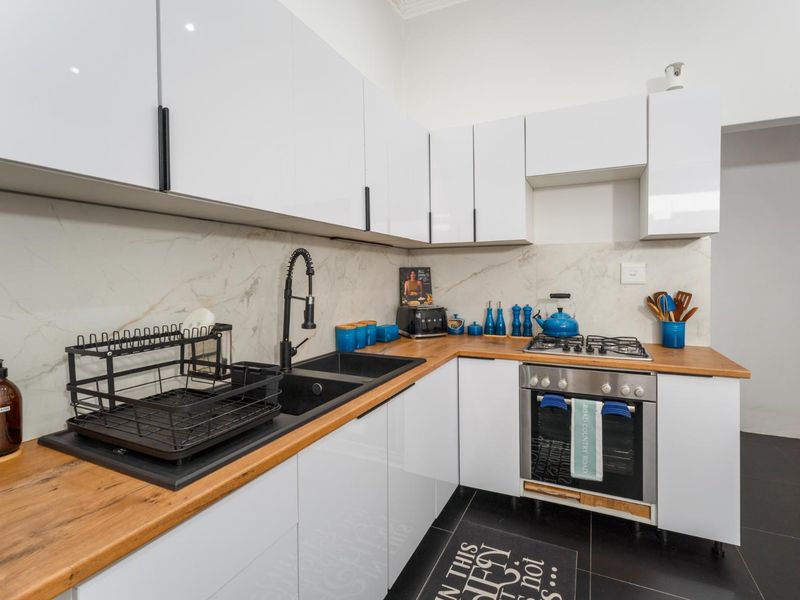 Modern kitchen featuring white gloss cabinetry, timber benchtops, marble-look splashback, and integrated stainless steel appliances including a gas cooktop and oven.