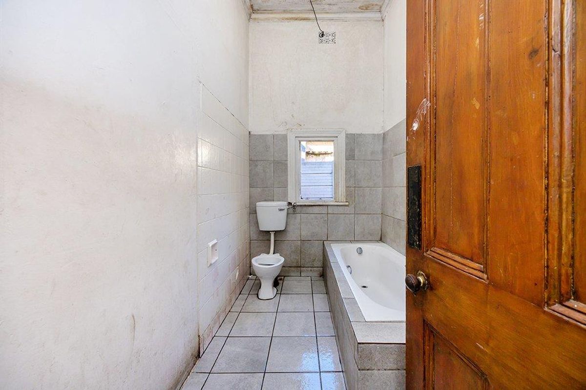 A dated bathroom featuring a built-in bathtub, toilet, and tiled flooring, requiring significant renovation and cosmetic updates to restore its functionality and appeal.