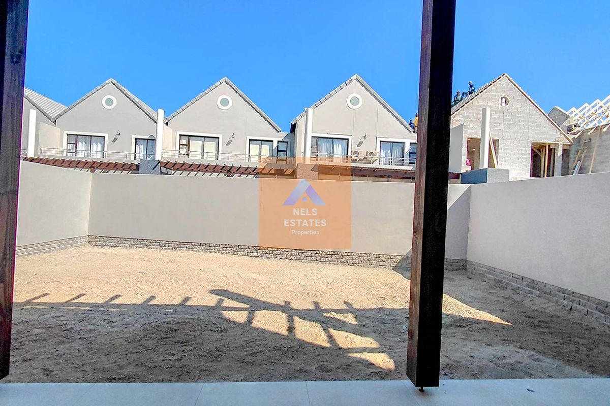 Rear view of a townhouse complex featuring a large, undeveloped backyard area with perimeter boundary walls and timber pergola supports.