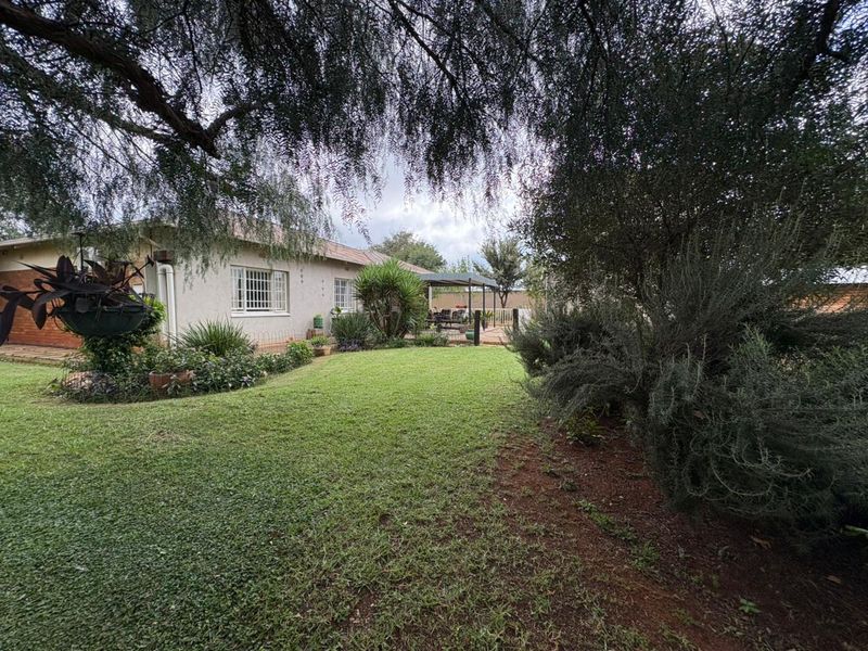 A spacious rear garden featuring a well-maintained lawn, mature trees, and a covered patio area attached to the rear of the house.