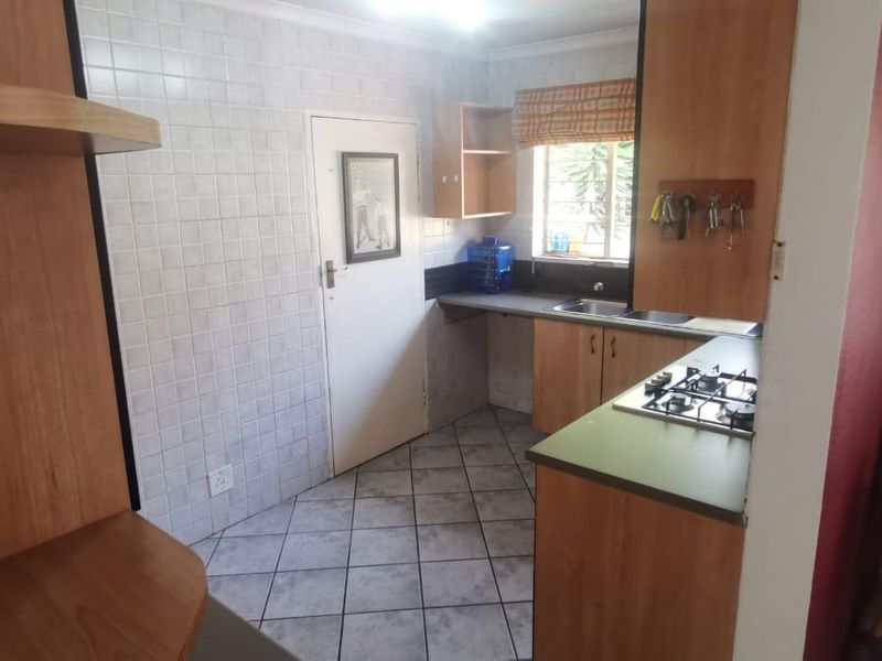 A functional kitchen featuring built-in wooden cabinetry, a gas hob, double sink, and tiled finishes throughout.