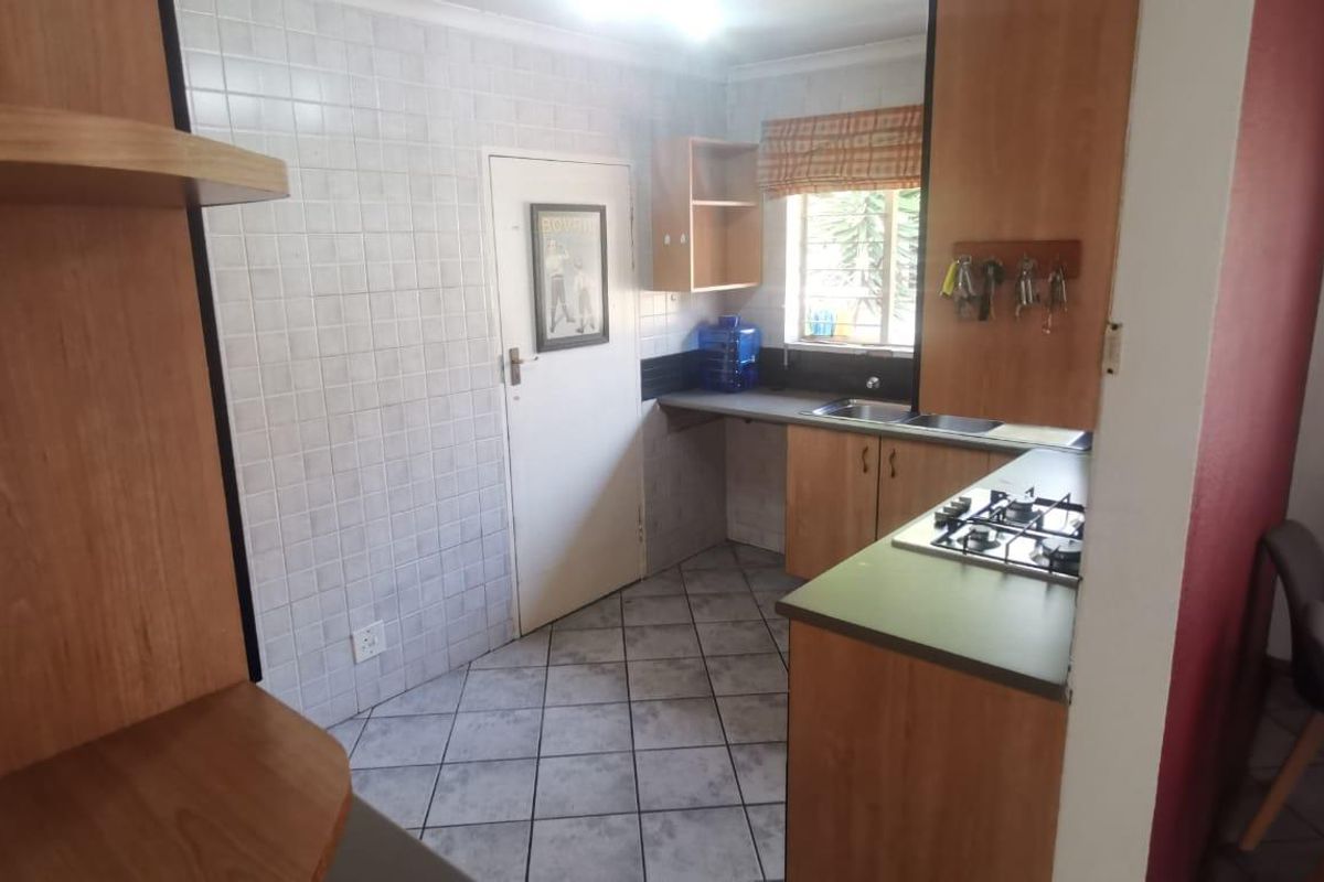 A functional kitchen featuring built-in wooden cabinetry, a gas hob, double sink, and tiled finishes throughout.