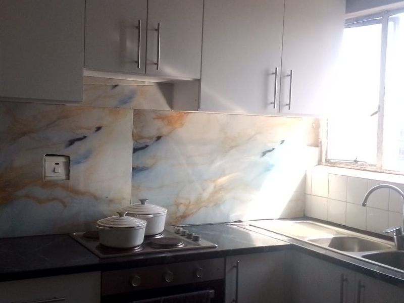 A functional kitchen featuring white cabinetry, a marble-effect splashback, integrated electric hob and oven, and a stainless steel double sink with a window view.