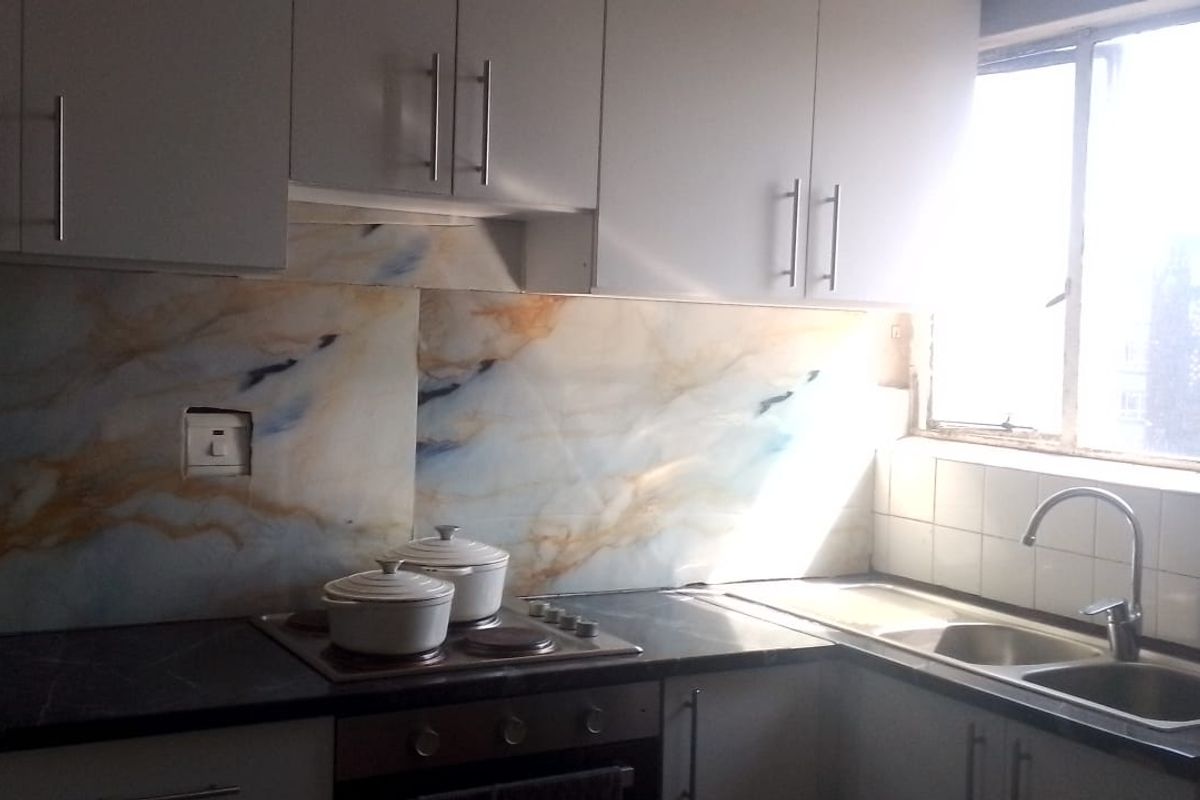 A functional kitchen featuring white cabinetry, a marble-effect splashback, integrated electric hob and oven, and a stainless steel double sink with a window view.