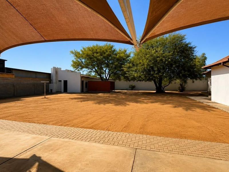 Spacious rear yard featuring a large paved patio area, shade sail covering, and established trees within a secure boundary wall perimeter.