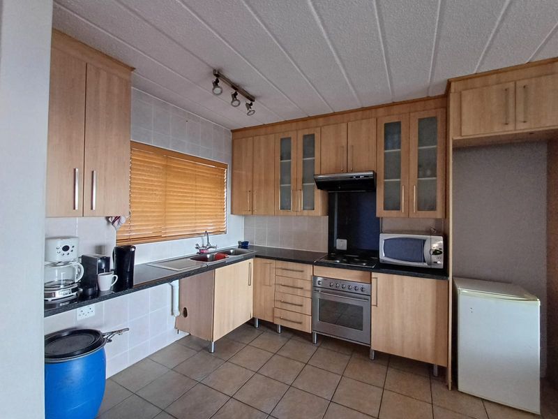 A functional kitchen featuring light wood cabinetry, tiled flooring, built-in oven with extractor fan, and a tiled backsplash with a window view.