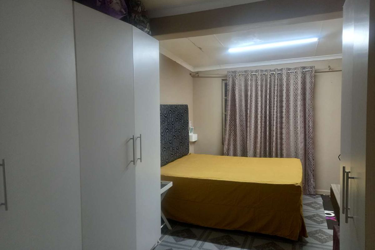 A bedroom featuring built-in wardrobes, tiled flooring, and a window with curtain treatments.