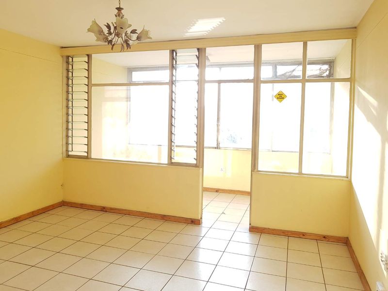 An empty living area featuring tiled floors, timber skirting, and a large glass partition wall with louver windows, offering a bright, open-plan layout.