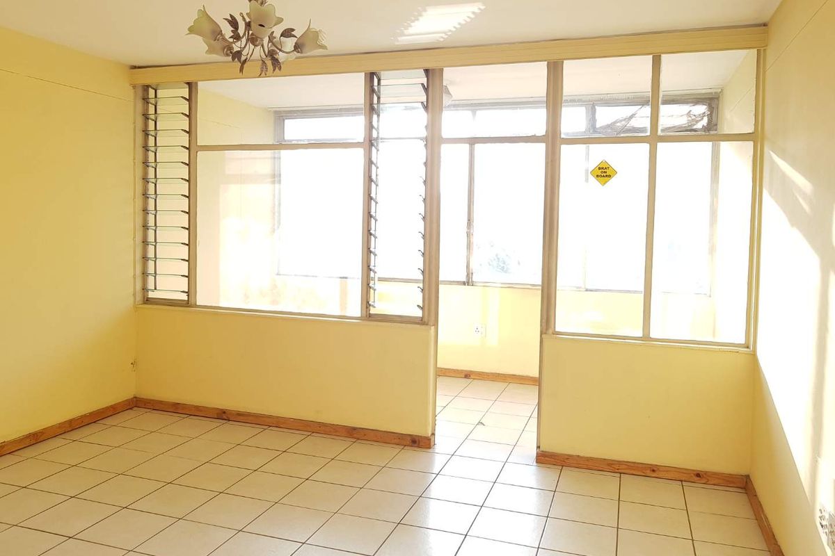 An empty living area featuring tiled floors, timber skirting, and a large glass partition wall with louver windows, offering a bright, open-plan layout.
