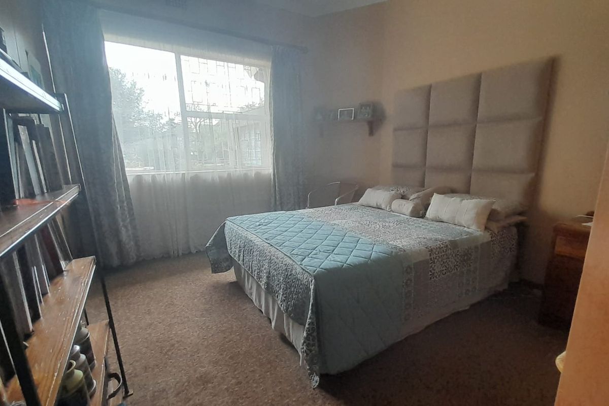 A bedroom featuring a large window with security bars, carpeted flooring, and a neutral wall finish.