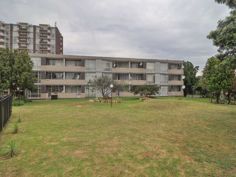 Rear view of a multi-story apartment complex featuring brick facade, sliding glass balcony doors, and a shared communal garden area.