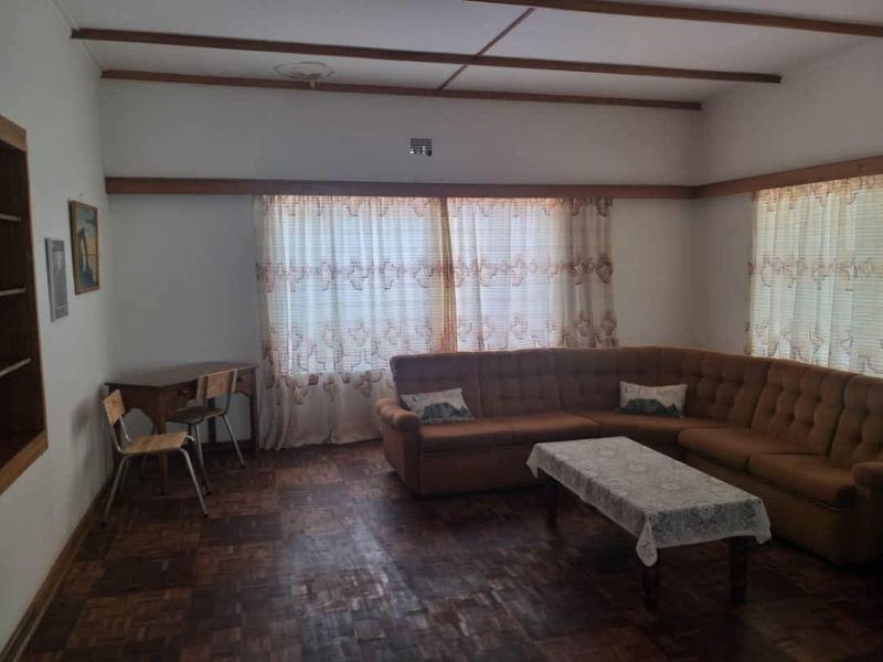 A spacious living room featuring classic parquet flooring, exposed timber ceiling beams, and a built-in shelving unit, offering a traditional aesthetic.