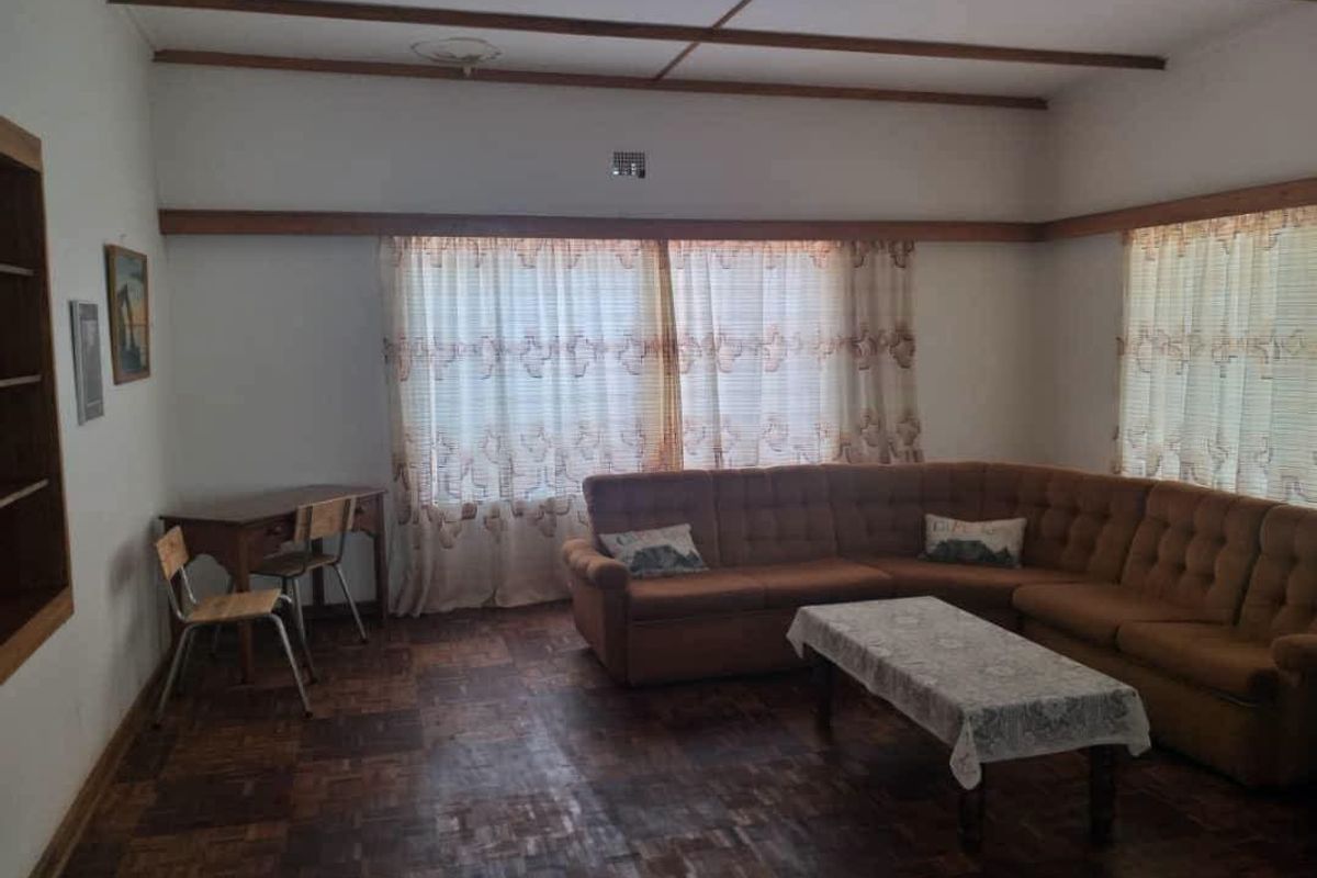 A spacious living room featuring classic parquet flooring, exposed timber ceiling beams, and a built-in shelving unit, offering a traditional aesthetic.