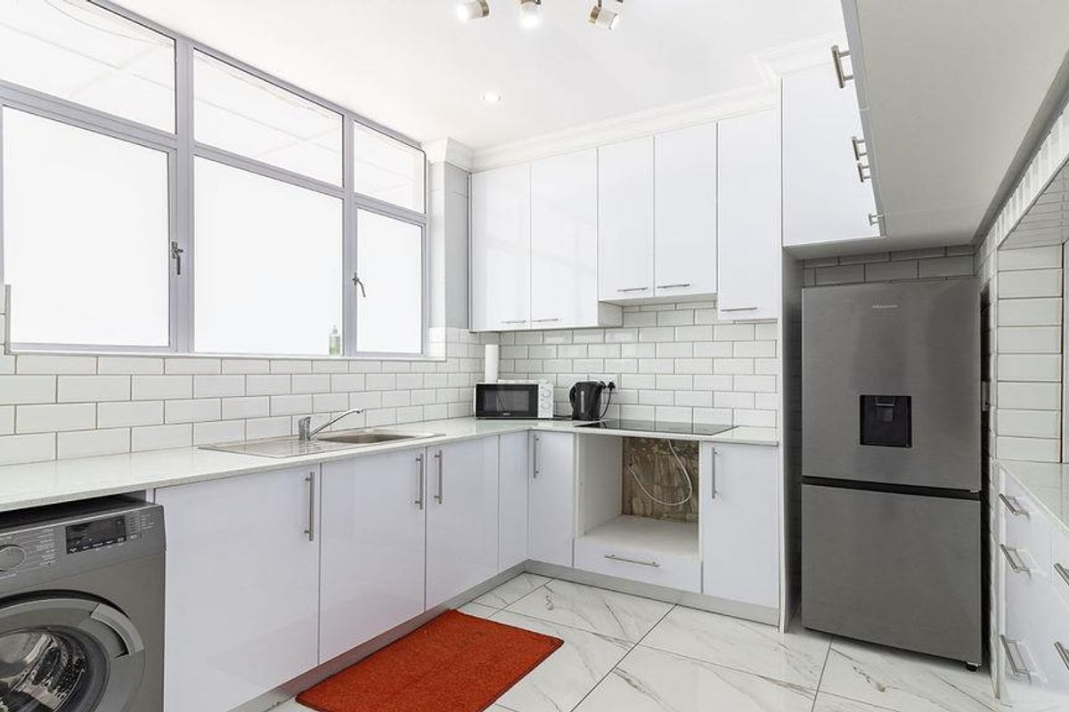Modern kitchen featuring white cabinetry, subway tile backsplash, stone countertops, and integrated plumbing for a washing machine.