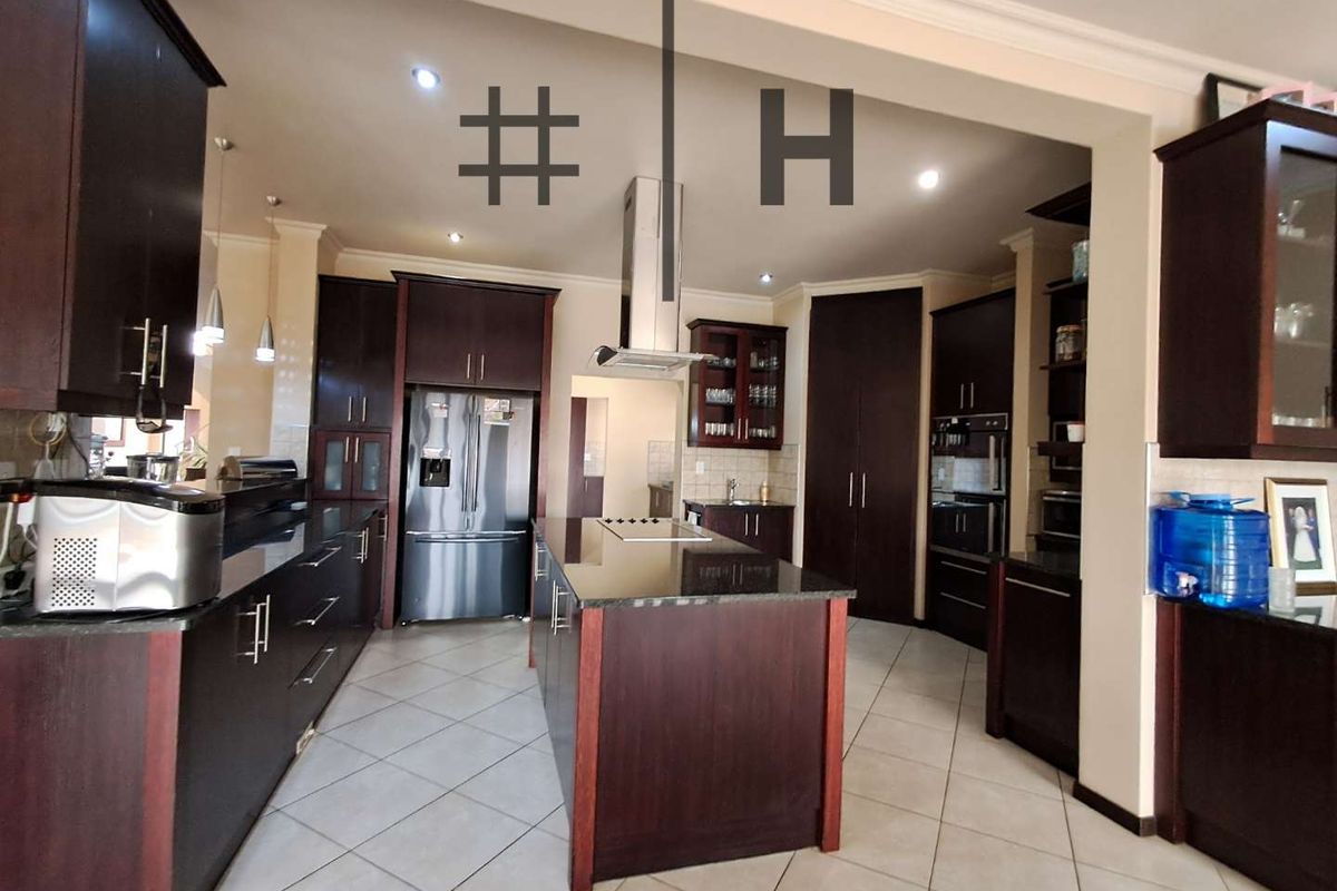 Spacious kitchen featuring dark wood cabinetry, granite countertops, a central island with a built-in cooktop, and stainless steel appliances.