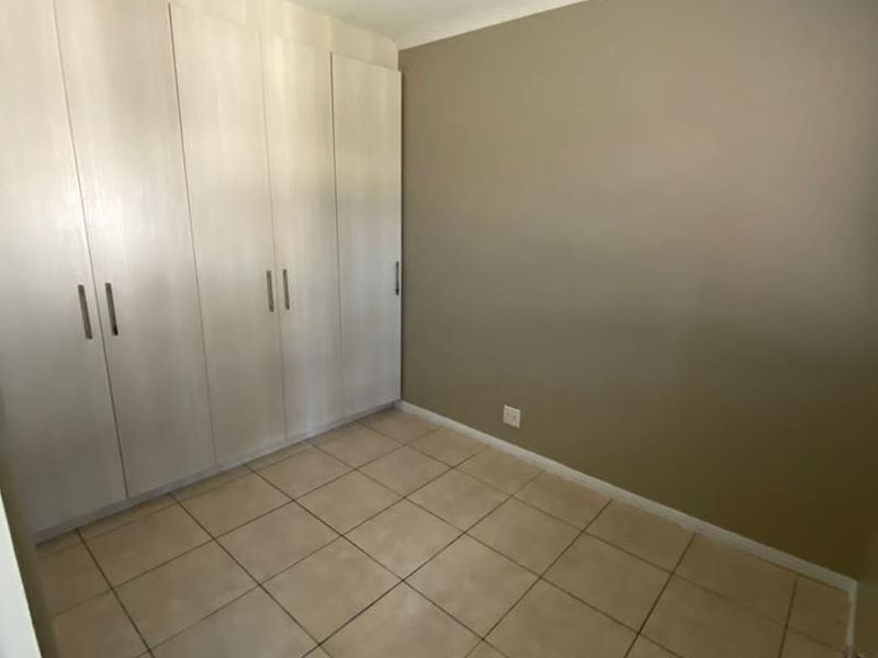 A clean, empty bedroom featuring neutral tiled flooring and ample built-in cupboard storage space.