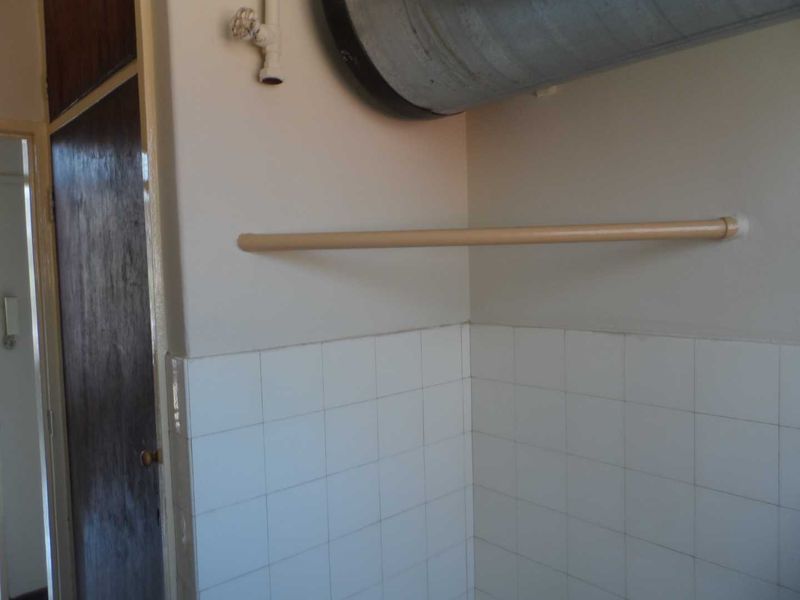 A functional laundry area featuring tiled splashbacks, exposed plumbing, and a wall-mounted rail for utility use.