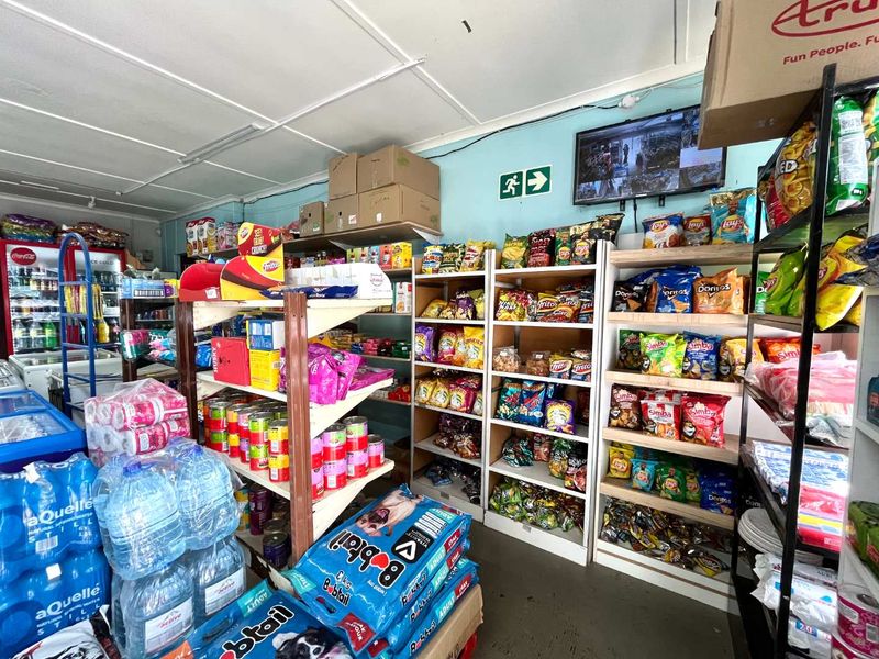 Interior view of a retail shop space featuring fixed shelving units and basic utility lighting, currently utilized for inventory storage and display.