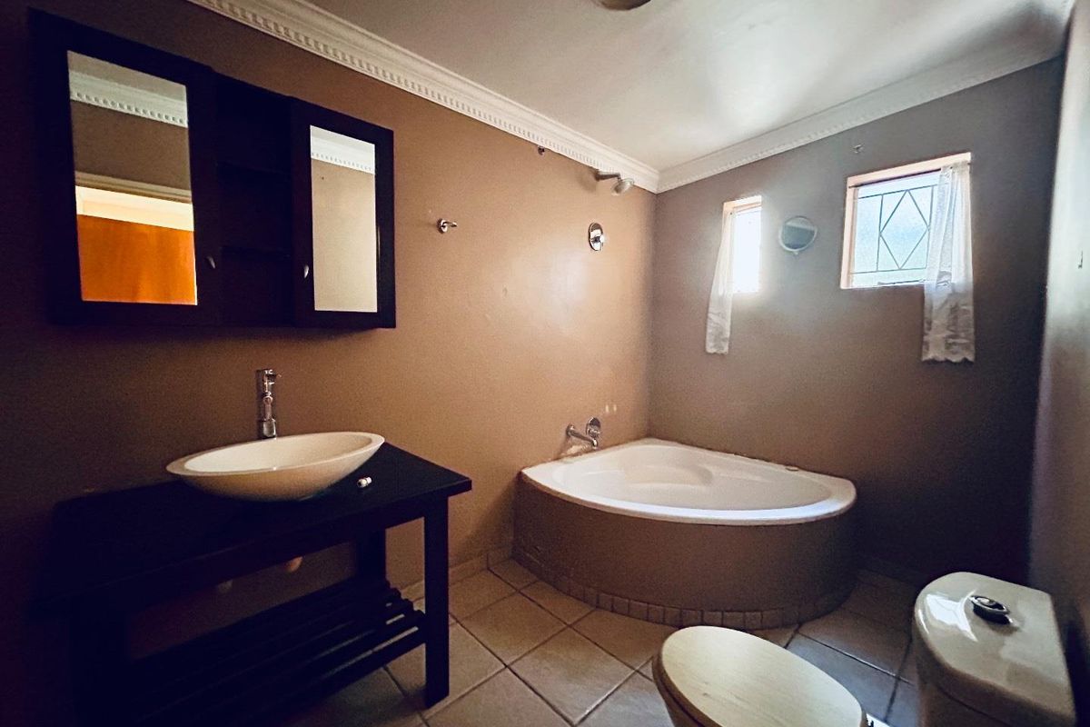 A functional bathroom featuring a corner bathtub, a vessel sink vanity, and a standard toilet with tiled flooring.