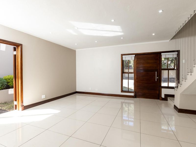 A bright, open-plan living area featuring polished tile flooring, recessed downlights, and a modern staircase balustrade, leading out to an exterior space.