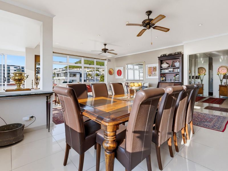 Spacious open-plan dining and living area featuring tiled floors, ceiling fans, and large windows with natural light and neighborhood views.