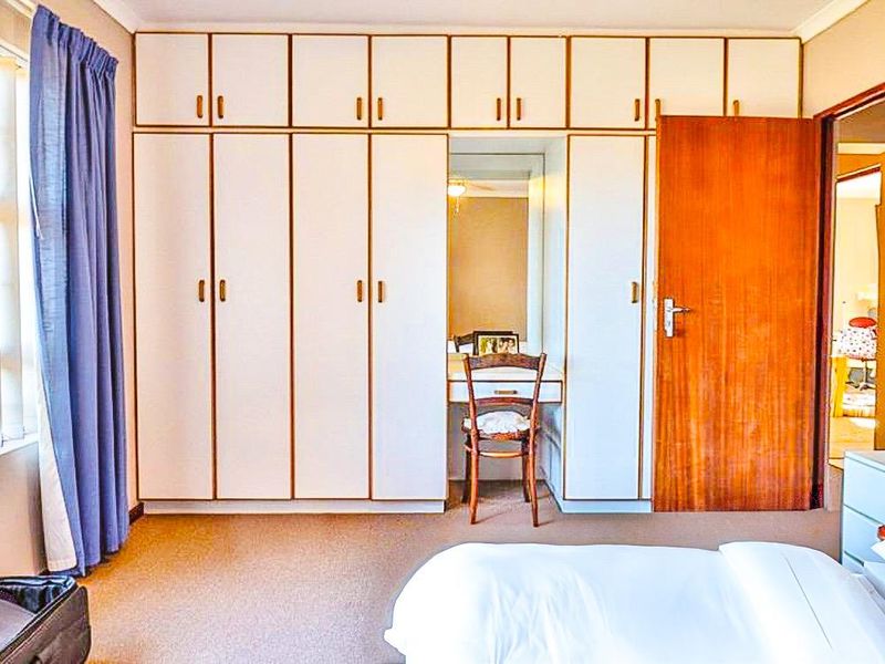 A bedroom featuring extensive built-in cupboards with an integrated vanity station, carpeted flooring, and natural light through vertical blinds.