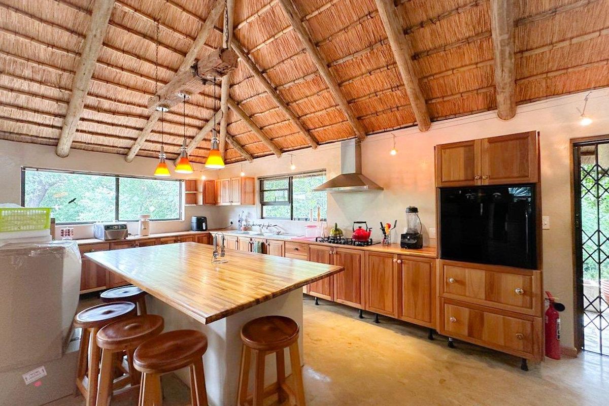 Spacious kitchen featuring a high vaulted thatched ceiling, wooden cabinetry, a central island with a timber countertop, and integrated stainless steel extractor fan.