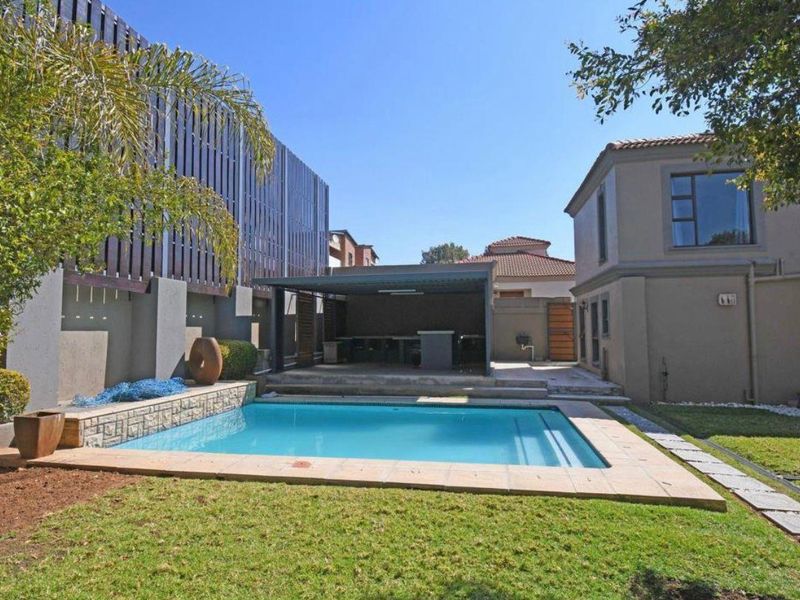 Outdoor entertainment area featuring a swimming pool, paved surround, and a covered patio with a built-in bar structure.
