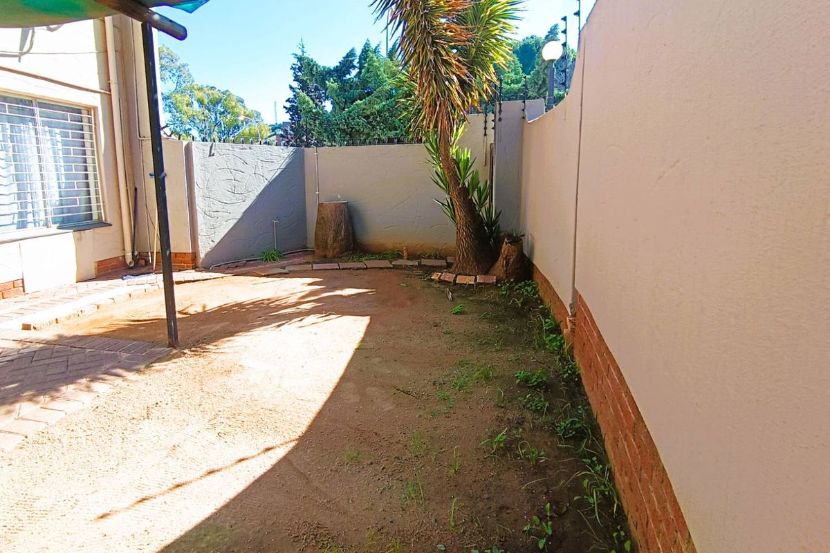 A private rear courtyard area featuring a paved section, perimeter boundary walls, and established garden elements.