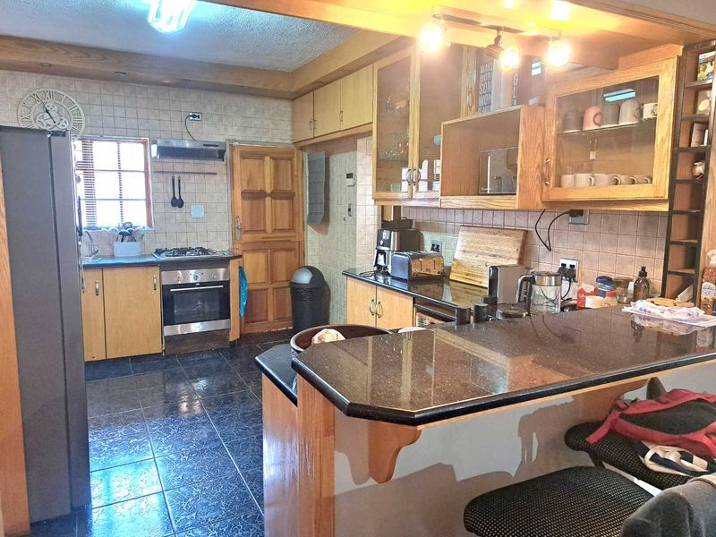 A functional kitchen featuring wooden cabinetry, granite countertops, a gas hob, and a breakfast bar, offering a practical layout with ample storage space.