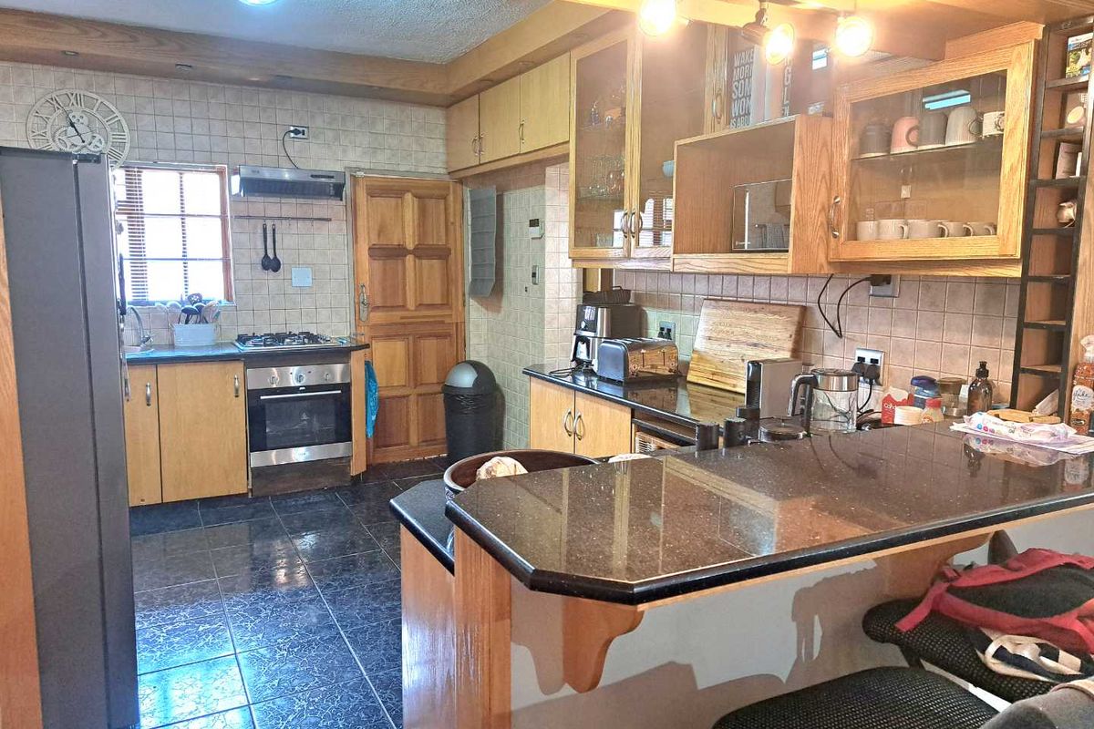 A functional kitchen featuring wooden cabinetry, granite countertops, a gas hob, and a breakfast bar, offering a practical layout with ample storage space.