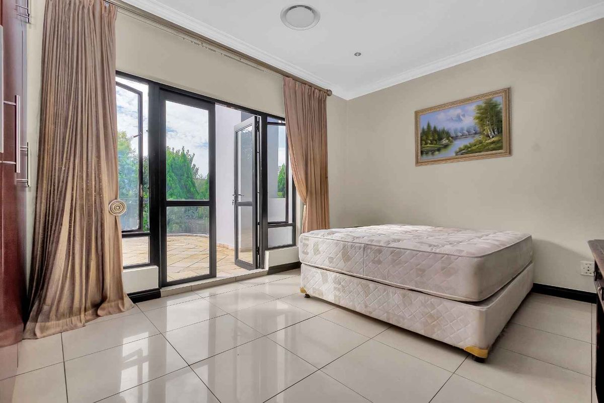 A bright bedroom featuring large aluminium-framed glass doors that open onto an outdoor patio, complemented by neutral tiled flooring and recessed lighting.