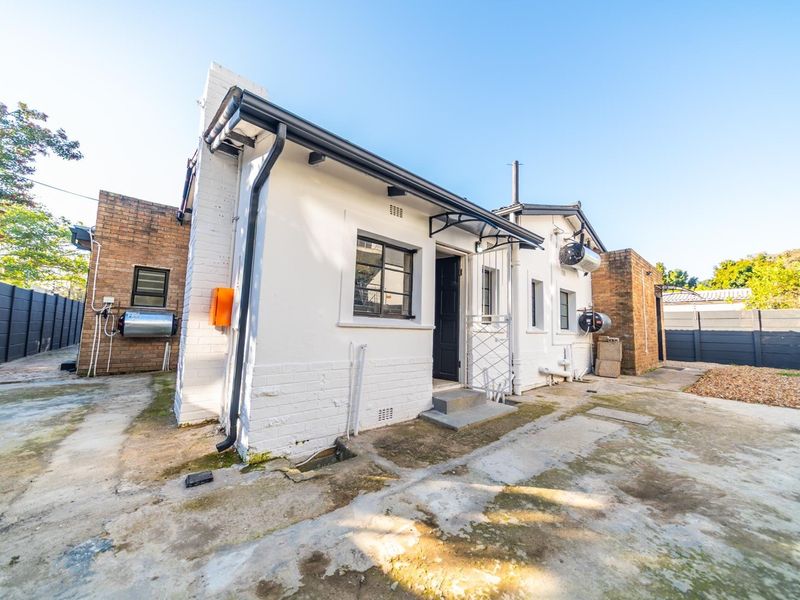 Rear exterior view of the apartment featuring a white painted brick facade, security gate, and concrete paved yard area.