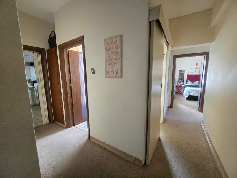 A functional apartment hallway connecting multiple rooms, featuring carpeted flooring and standard wooden door frames throughout the space.