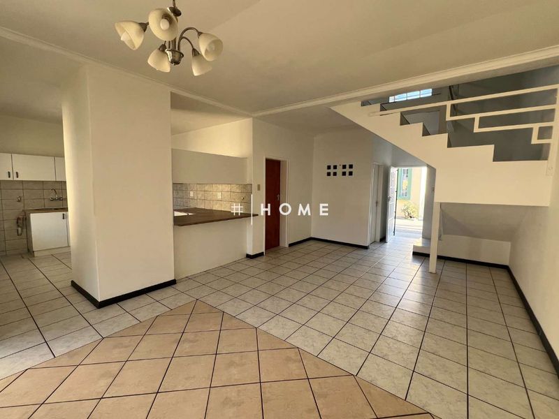 Spacious open-plan living area featuring tiled flooring, a staircase, and an adjoining kitchen with built-in cabinetry and countertops.
