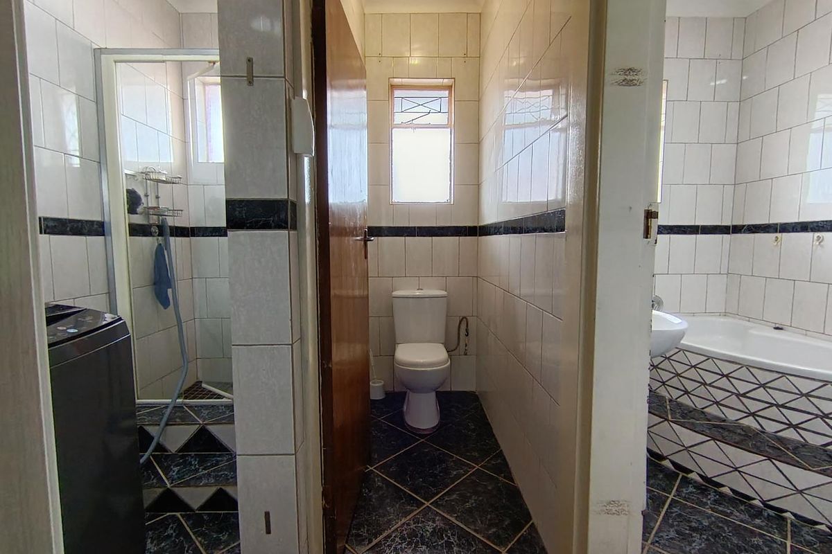 A functional bathroom featuring a separate shower cubicle, a central toilet, and a bathtub with tiled surround and dark floor tiling.