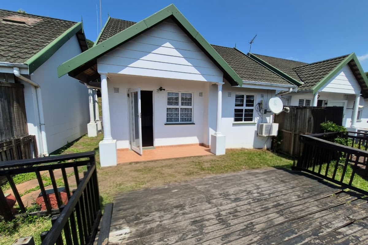 Rear view of a townhouse featuring a covered patio, timber decking, and a small garden area with established fencing.