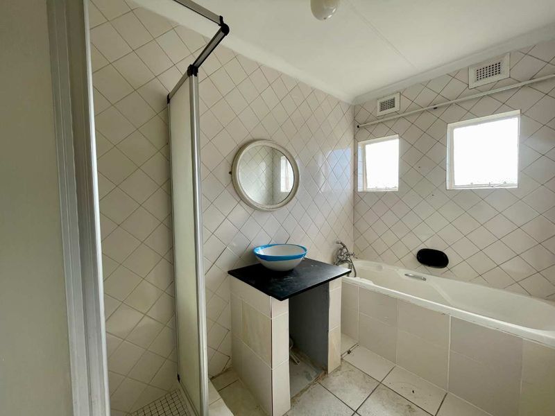 A dated bathroom featuring a bathtub, shower enclosure, and a vanity base. The space requires cosmetic updates and finishing to reach its full potential.