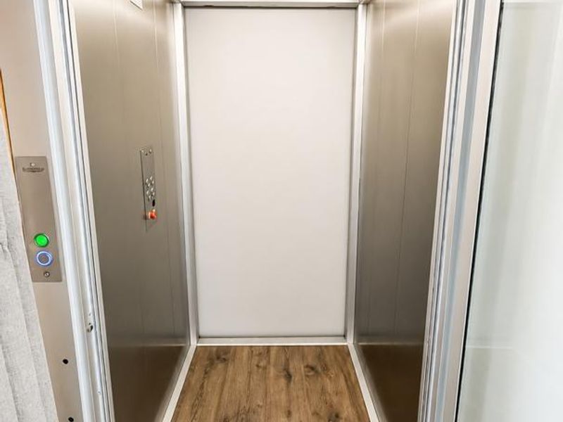 A modern, well-maintained residential elevator featuring metal wall panels, integrated LED lighting, and wood-look flooring.