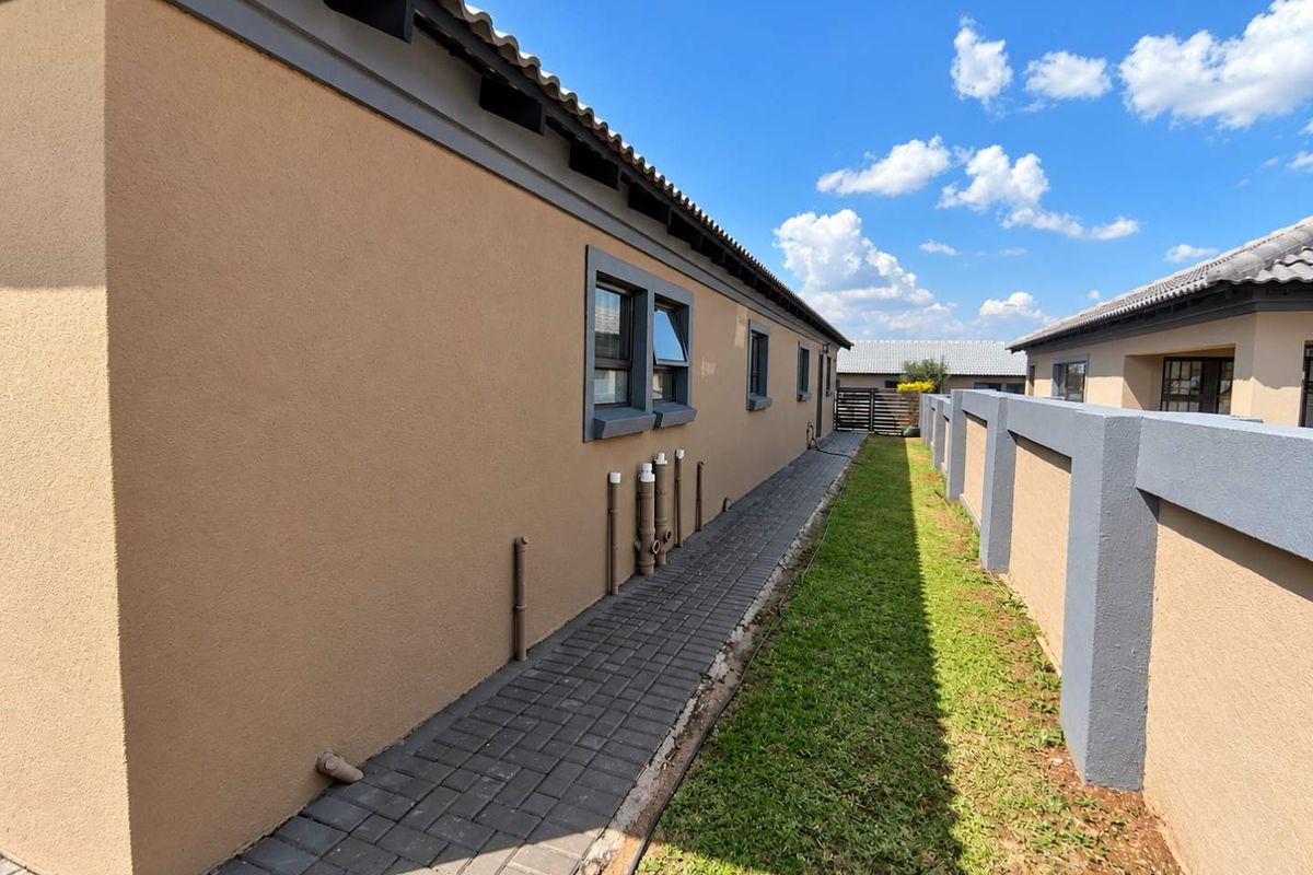 A side view of the townhouse exterior featuring a paved walkway, a small grass strip, and a secure boundary wall.