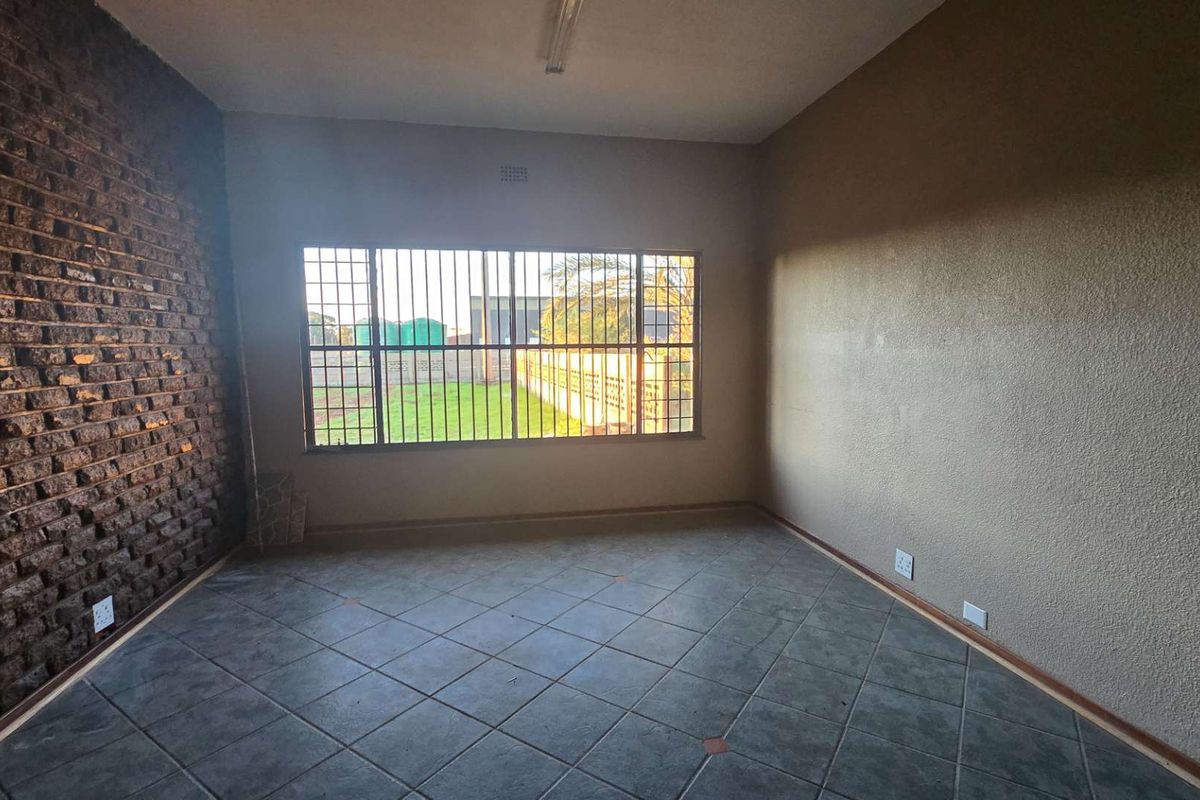 An empty room featuring a textured brick accent wall, tiled flooring, and a large window fitted with security bars.