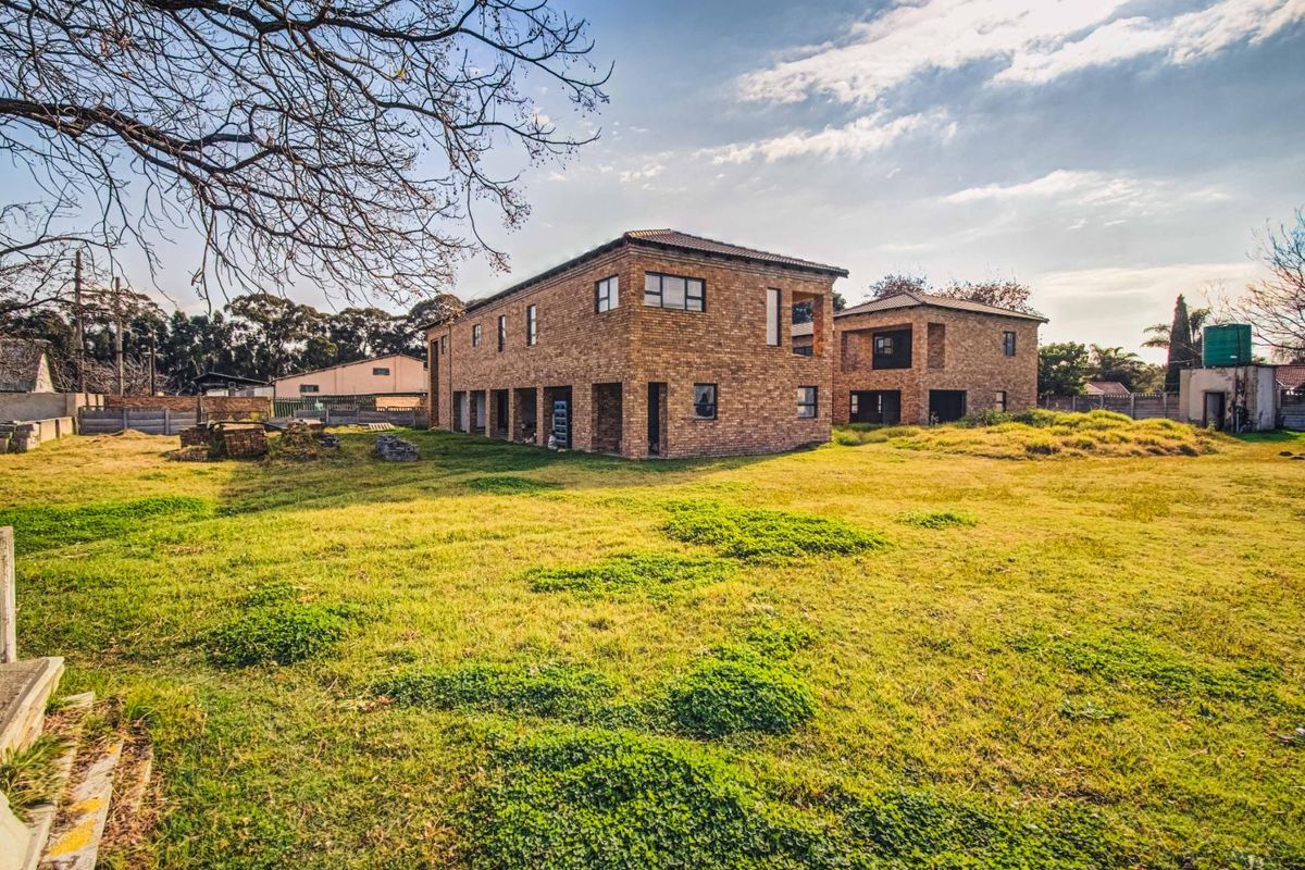 A view of the rear exterior of the face-brick property, featuring multi-level structures, concrete pillars, and an expansive, undeveloped garden area.