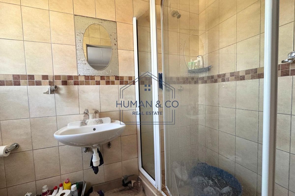 A functional bathroom featuring a wall-mounted basin and a glass-enclosed shower with tiled walls and decorative border accents.