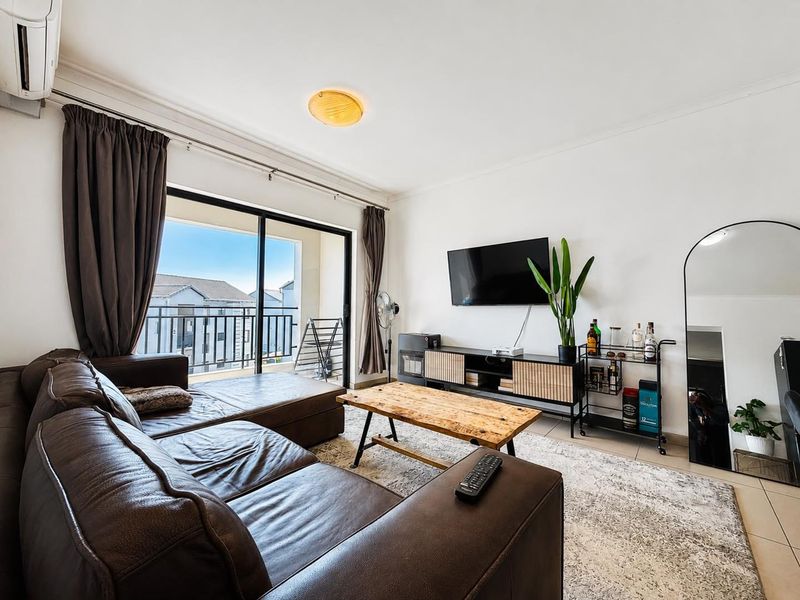 A well-lit living room featuring tiled flooring, an air conditioning unit, and a large sliding glass door providing access to a balcony.