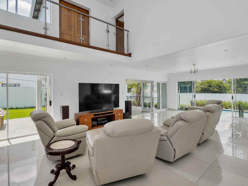 Spacious double-volume living area featuring polished tile floors, glass balustrades, and large sliding doors providing seamless access to the outdoor patio and pool area.