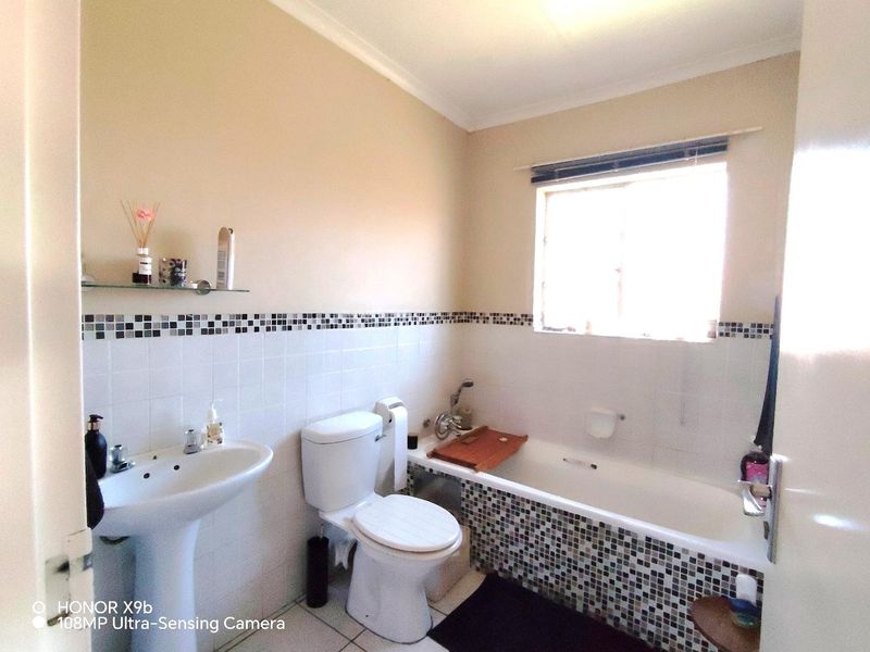 A functional bathroom featuring a pedestal basin, toilet, and bathtub with decorative mosaic tile accents and a window for natural light.